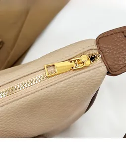 Detail of beige pebbled leather texture with smooth light gold metal zipper puller