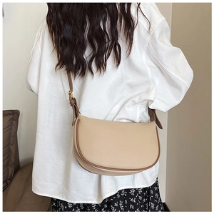 Detail view of beige saddle bag with brown trim and golden metal strap buckle adjustment