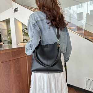 Large black matte bucket bag with wide strap shown on model in a casual setting