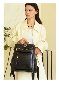 Close-up of black leather backpack with gold zippers and tassel detail on model