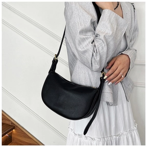 Detail of black lychee grain leather crescent bag with golden hardware on a shoulder