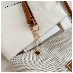 Detail einer cremefarbenen Canvas-Tasche mit braunem Lederriemen und Goldkette