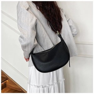 Detail of black pebbled leather dumpling bag worn as a shoulder bag on a grey blazer