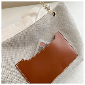 Detail der beigen Canvas-Tragetasche mit brauner Ledertasche und goldenen Kettengliedern