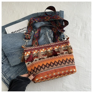 Detail of bohemian straw bucket bag showing colorful tassels and patterned wide strap