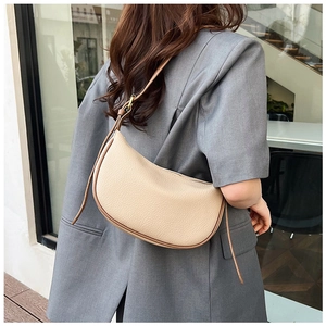 Detail of beige crescent hobo bag in lychee texture leather worn over a grey blazer