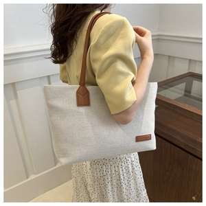 Detail of cream canvas tote bag with brown leather straps and fashion label tag