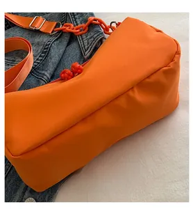 Detail of orange nylon shoulder bag with plastic chain strap and decorative zipper pulls