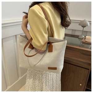 Detail of cream canvas tote bag featuring brown leather straps and a stylish leather patch