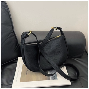 Detail of black pebbled leather half-moon bag with gold zippers on a leather sofa