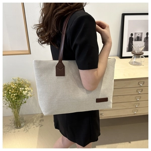 Detail view of canvas tote bag with brown leather handle on a female model