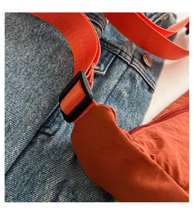 Detail einer orangen Nylontasche mit breitem Stoffgurt und Schnalle auf Denim-Hintergrund