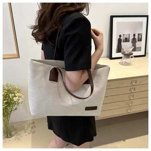 Detailed side view of large canvas tote bag with brown leather straps worn by a model
