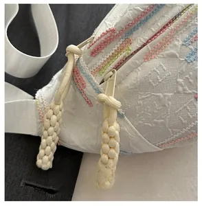 Détail d'un sac bandoulière blanc avec broderie colorée et tirette tissée