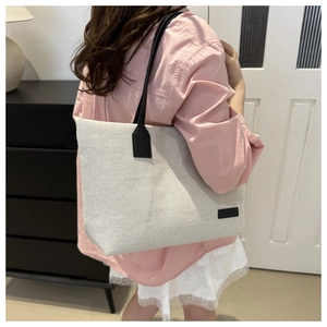 Detail of a large canvas tote bag with black leather handles shown on a model's shoulder