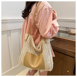 Model wearing a large beige straw woven tote bag with brown leather pocket detail