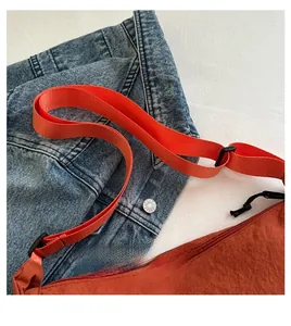 Detail der orangefarbenen Nylon-Halbmondtasche mit breitem Gurt auf Jeansjacke