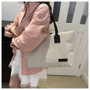 Detail of canvas tote bag featuring black shoulder strap and fashion label on the front