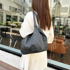 Minimalist black tote bag with long handles shown in a lifestyle urban setting