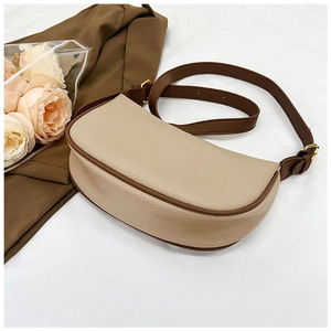 Detail of beige saddle bag with brown trim and golden hardware on white fabric