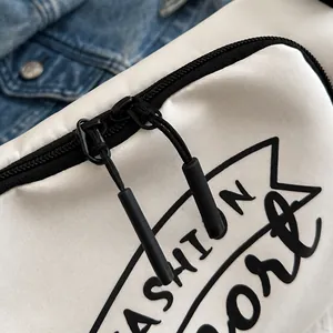Détail d'une double fermeture éclair fluide avec tirettes noires sur un sac sport blanc