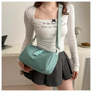 Detail view of light green nylon crossbody bag showing cylindrical shape and braided zipper pull