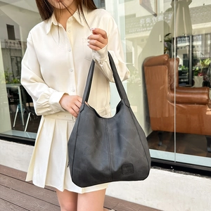 Detail of a large black vintage tote bag with square embossed logo and textured leather