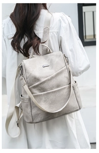 Detail of beige soft leather backpack showing multi-pocket design on model's back