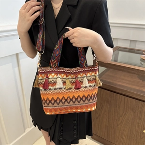 Ethnic straw bucket bag with colorful tassels and geometric strap worn by model