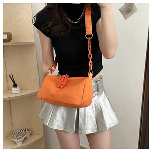Detail view of bright orange nylon crossbody bag with stylish chain on casual model outfit