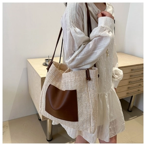 Detail of bohemian straw tote bag featuring a brown leather front pocket and slim straps