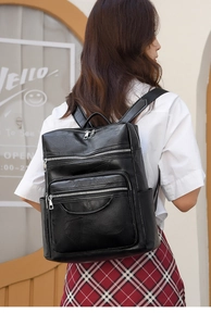 Detail of a vintage black leather backpack with multiple zipper pockets on a female model