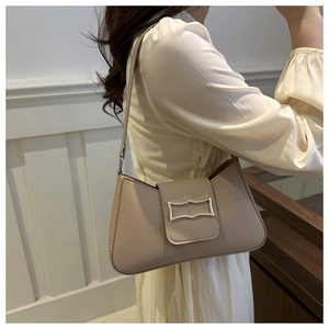 Detail of elegant beige shoulder bag with golden wave-patterned buckle and smooth texture