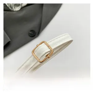 Detail of white leather shoulder strap with polished gold metal buckle and stitching