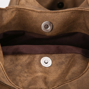 Close-up of magnetic snap closure on vintage brown canvas tote bag with multi-compartments