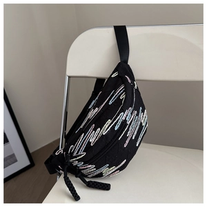 Détail du sac bandoulière noir avec broderie vagues arc-en-ciel sur une chaise blanche