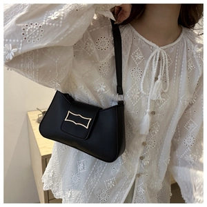 Close-up of black matte leather shoulder bag featuring a modern gold metal clasp on a white shirt