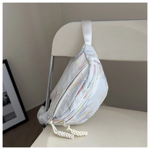 Vue latérale du sac bandoulière blanc avec broderie aux tons macaron sur une chaise blanche