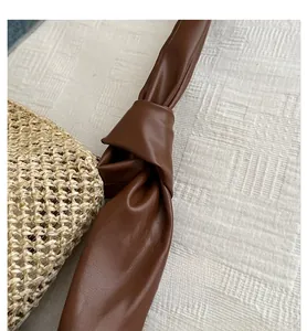 Detail of straw tote bag showing brown leather strap with unique knot design element