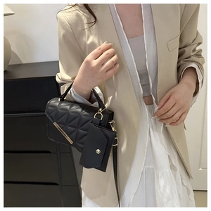 Detail of black quilted crossbody bag with gold hardware worn with beige blazer