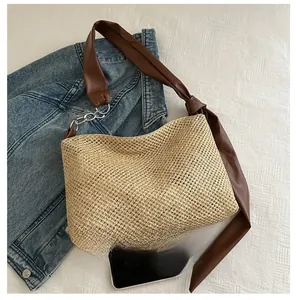 Detail of woven straw tote bag with brown faux leather strap and metal chain