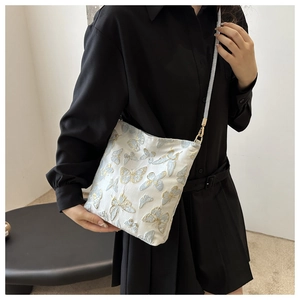 Close-up of white bucket bag featuring intricate blue and gold butterfly embroidery