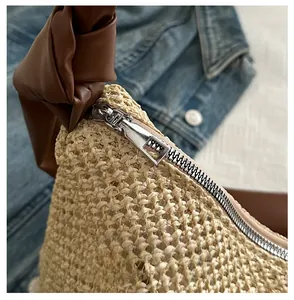 Detail of smooth metal zipper and brown leather handle on woven straw tote bag