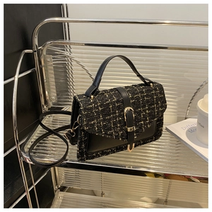 Close-up of elegant black tweed crossbody bag with gold buckle on a stylish shelf