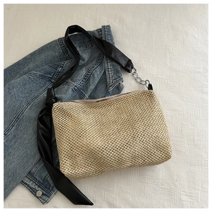 Close-up of woven straw tote bag featuring a black satin bow and metal chain strap