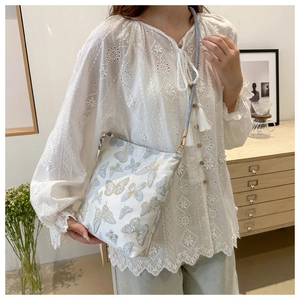 Detail of elegant butterfly embroidery on white bucket bag with a slim gray shoulder strap