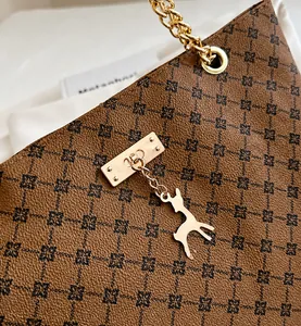 Dettaglio borsa shopper marrone con monogramma, catena dorata e ciondolo a cervo