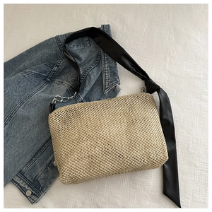 Detail of beige woven straw tote bag featuring black satin ribbon and silver chain straps