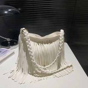 White faux leather crossbody bag with long tassels and woven strap on a modern desk