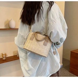 Détail d'un sac cabas tissé beige avec poignées en cuir marron porté par un mannequin